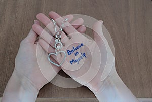 Phrase BELIEVE IN MYSELF written on the palm of a woman`s hand holding a silver bracelet with a heart