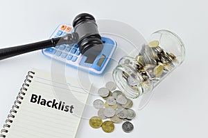 Phrase BLACKLIST written on notebook with judge gavel, calculator and coins