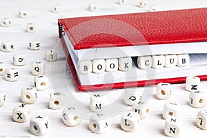 Phrase Book club written in wooden blocks in red notebook on white wooden table.
