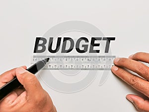 Phrase BUDGET written on white background with plastic ruler and hands holding marker pen.