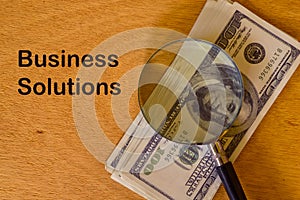 Phrase BUSINESS SOLUTIONS written on board with magnifying glass and money banknotes
