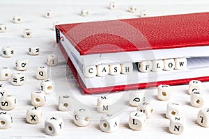 Phrase Cash flow written in wooden blocks in red notebook on white wooden table.