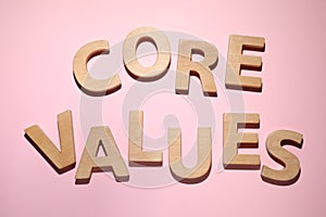 Phrase CORE VALUES made of wooden letters on pink background, flat lay
