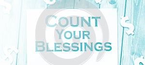 The phrase Count Your Blessings typed on a piece of paper and paper dollar signs around. Career concept