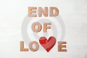 Phrase `End of love` with torn cardboard heart and letters on light background, top view