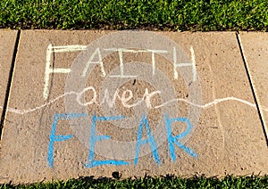 The phrase `Faith over Fear` written with sidewalk chalk on gray concrete pavement background
