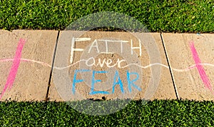 The phrase `Faith over Fear` written with sidewalk chalk on gray concrete pavement background