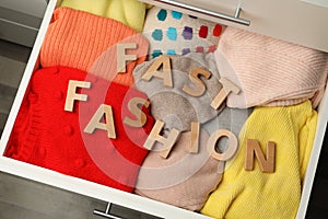 Phrase FAST FASHION made of wooden letters and different clothes in open drawer, top view