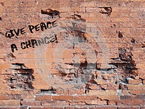 Phrase Give Peace a Chance spray painted in white on a damaged brick wall