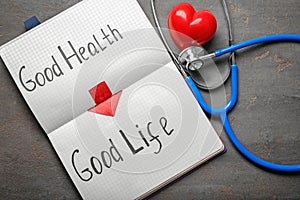 Phrase Good health - good life written in notebook with stethoscope on grey background