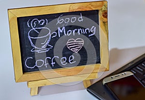 Phrase Good Morning coffee written on a chalkboard on it and smartphone, laptop