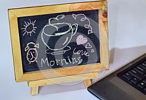 Phrase Good Morning coffee written on a chalkboard on it and smartphone, laptop