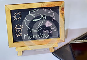 Phrase Good Morning coffee written on a chalkboard on it and smartphone, laptop