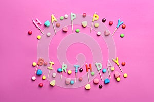 Phrase HAPPY BIRTHDAY made of candles and candies on color background