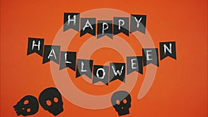 Phrase happy halloween with black skulls on an orange background. Stop motion