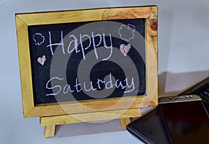 Phrase Happy saturday written on a chalkboard on it and smartphone, laptop