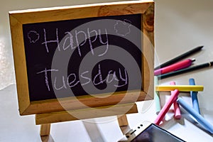 Phrase happy tuesday written on a chalkboard on it and smartphone, colorful chalk.