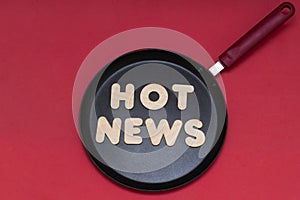 Phrase hot news from wooden letters on a frying pan, red background. News preparation concept. The photo