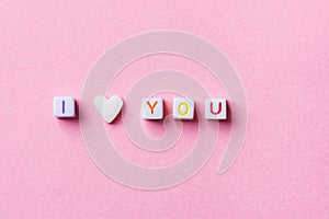 Phrase I Love You Made from Letter Cubes and Single Heart Shape White Sugar Candy Sprinkle on Pink Background. Romance Valentines