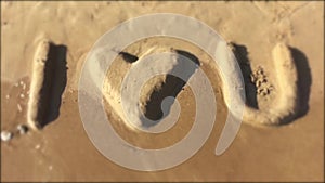 Phrase I Love You made of sand on the seaside, washes by the sea wave. Blur on top and bottom, place for text. Slow motion. Fun Lo