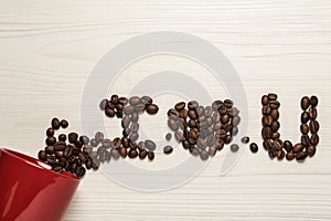 Phrase I Love You made of scattered coffee beans from red cup on white wooden table, flat lay