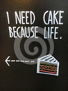 Phrase `I need cake because life` on advertising black board on the street.