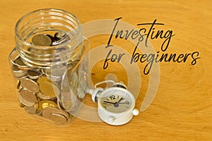 Phrase INVESTING FOR BEGINNERS written on board with clock and coins. Business concept. Selective focus