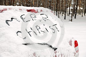 Phrase `Merry Christmas` written on snow covered car in winter forest.