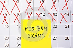 The phrase Midterm exams written on a yellow sticky note posted on a calendar or planner page as a reminder. Closeup of a personal photo