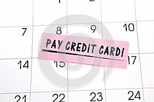 The phrase Pay off Credit cards written in black text on a pink sticky note posted to a calendar page as a reminder. Close up of a
