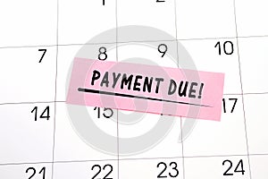 The phrase Payment Due written in black text on a pink sticky note posted to a calendar page as a reminder. Close up of a personal