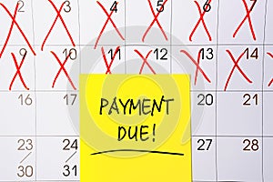 The phrase Payment Due written in black text on a yellow sticky note posted to a calendar page as a reminder. Close up of a