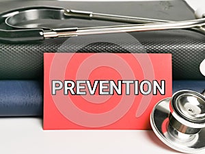 Phrase PREVENTION written on red paper card with stethoscope and books.