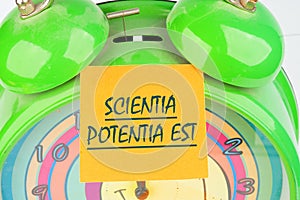 the phrase Scientia Potentia Est (Knowledge is power) written in Latin on the orange sticker on the alarm clock