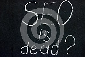 The phrase `SEO is dead?` on a dark background chalk boards. An important issue for the younger generation of copywriters