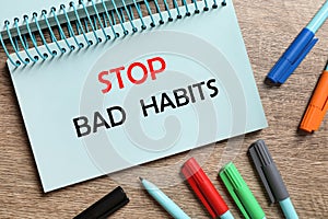 Phrase Stop Bad Habits in notebook and pens on wooden table, flat lay