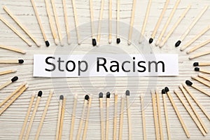 Phrase Stop Racism and different matches on white wooden table, flat lay