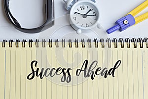 Phrase SUCCESS AHEAD written on notebook with clock, watch and math compass
