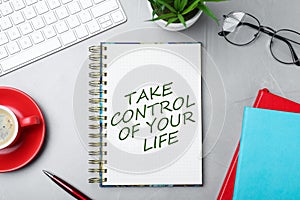 Phrase Take Control of Your Life in notebook, office stationery and cup of coffee on light grey table, flat lay