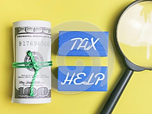 phrase TAX HELP with wooden cubes,dollar bills and magnifying glass over yellow background.