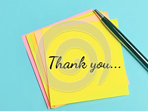 Phrase THANK YOU written on sticky note with a pen.