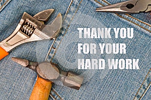 Phrase THANK YOU FOR YOUR HARD WORK written on blue jeans with hammer, wrench and pliers