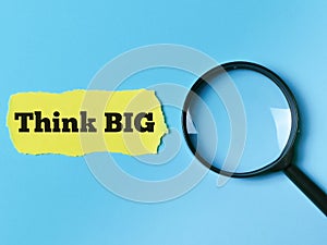 Phrase think big on yellow paper strip with magnifying glass.