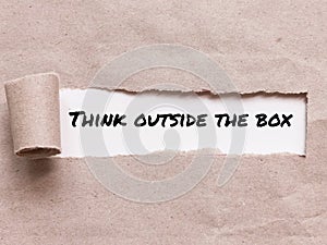 Phrase THINK OUTSIDE THE BOX appearing behind torn brown paper.