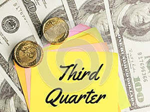 Phrase Third Quarter written on sticky note with fake money and coins.
