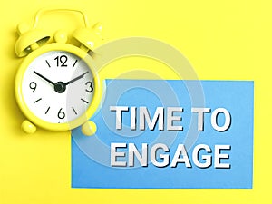 Phrase TIME TO ENGAGE written on blue card with alarm clock over yellow background.