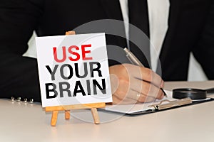 The phrase Use Your Brain in blue text on an index card pinned to a cork notice board as a reminder