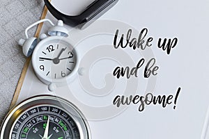 Phrase WAKE UP AND BE AWESOME! written on notebook with clock, watch and compass