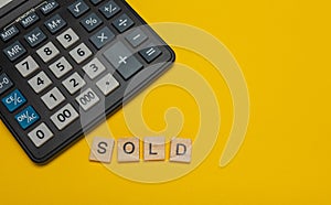 Phrase or word - sold. Wooden block letter word and modern calculator on a yellow background, business concept with space for text