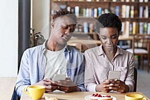 Phubbing problem. Black couple stuck in their smartphones on boring date at cafe photo